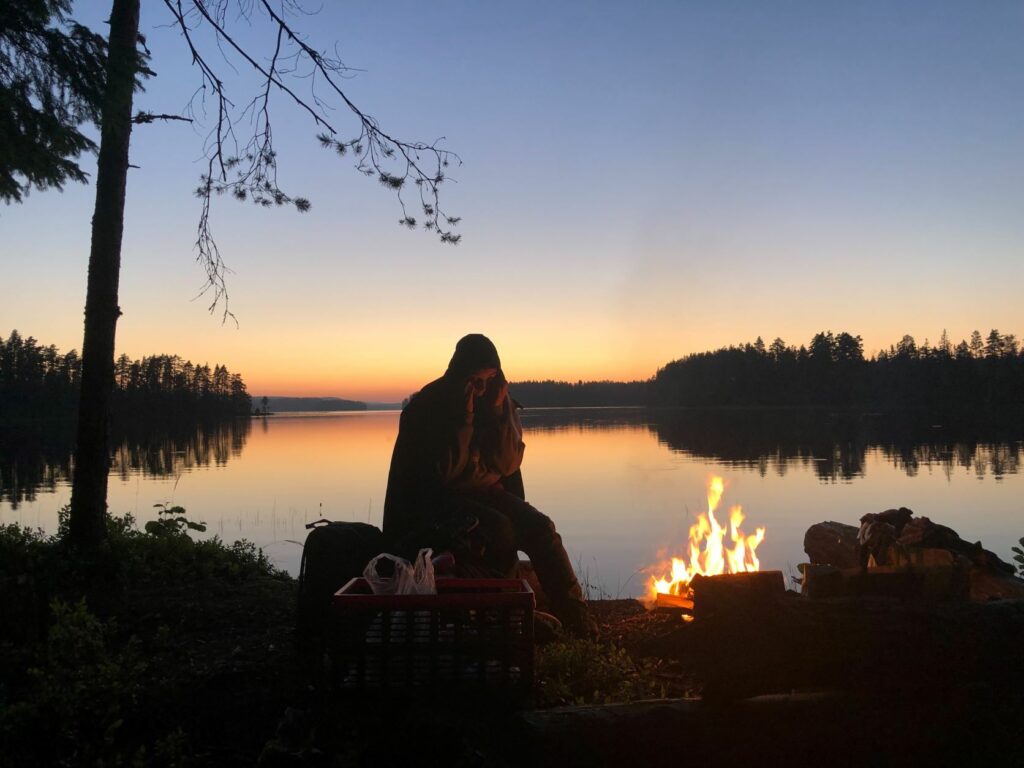 Person vid eld i solnedgång bredvid sjö